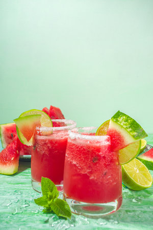 Cold summer cocktail, watermelon margaritas or mojito with watermelon and lime slices, crushed ice and mint. Seasonal refreshing drink, on bright green sun lighted backgroundの写真素材