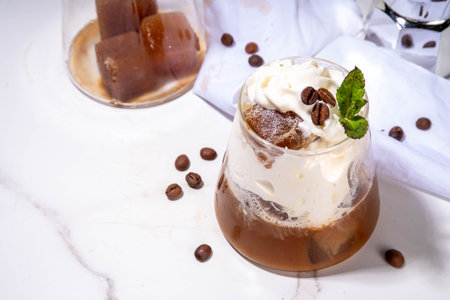 Latte coffee summer cocktail. Cold brewed iced cappuccino coffee,  with whipped foamy cream or non-dairy milk and frozen coffee ice cubes, on white kitchen background copy spaceの写真素材