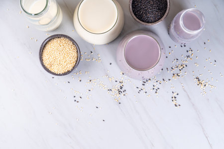 Black and white sesame milk, Alternative vegan non-dairy milk drink on glass and bottles with sesame seeds on light stone background. Raw food, vegetarian natural organic food dietの写真素材