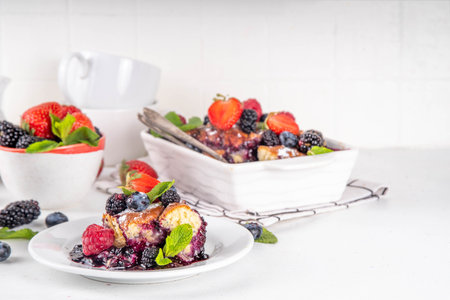 Homemade sweet berry cobbler pie cake with various garden forest berries - strawberry, blackberry, blueberry, healthy summer dessert recipe in baking pan and plate, copy spaceの写真素材