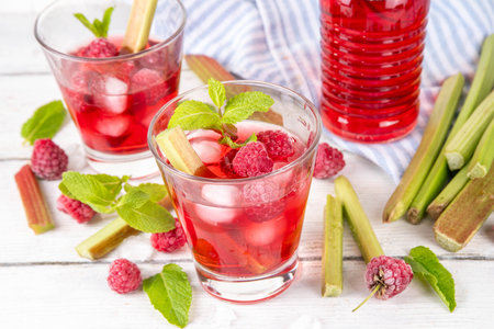 Raspberry rhubarb iced tea, lemonade or mojito. Cold summer fruit refreshment drink with rhubarb syrup, raspberry and mint, on white wooden tableの写真素材