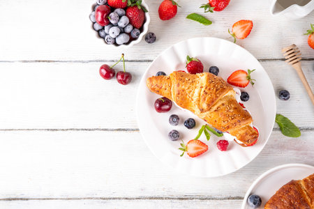 Sweet breakfast croissant sandwich with whipped cream, fresh fruit and berry. Tasty summer lunch or snack with fresh baked croissant, filled with strawberry, blueberry, cherry, raspberry, nutsの写真素材
