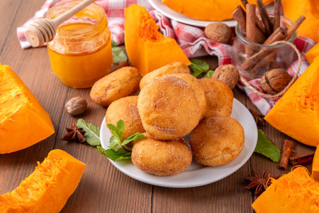Autumn pumpkin pie donuts with cinnamon sugar sprinkled topping and pumpkin spice filling, on white wooden table with honey and pumpkin squash slices, copy spaceの写真素材