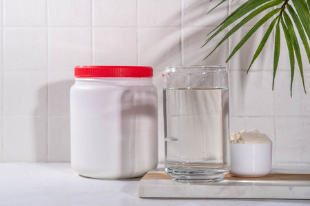 Collagen protein powder with glass of water on white kitchen table. Natural supplement for beauty, health of skin, bones, joints and intestines,  anti-age conceptの写真素材