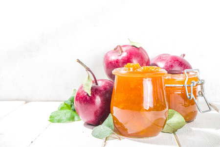 Homemade golden colored apple jam, with farm red apples and leaves on white wooden background copy spaceの写真素材