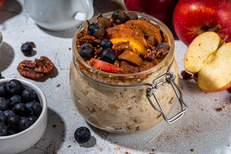 Healthy vegan dietary breakfast or snack. Apple pie overnight oatmeal, oats flakes with apples, yogurt, cinnamon, spices, blueberry. In glass, on a white marble table. Copy spaceの写真素材