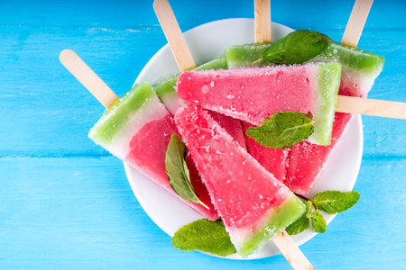 Tasty sweet watermelon ice cream lollies on blue wooden table, top view. Summer vacation and holiday background with watermelon fruit popsicles, top view copy spaceの写真素材