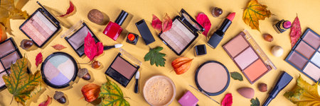 Autumn make up set on golden table background, with autumn leaves and beauty accessories. Various makeup professional cosmetics - shadows, lipstick, corrector, mascara, eyeliner, bronzer, blushの写真素材