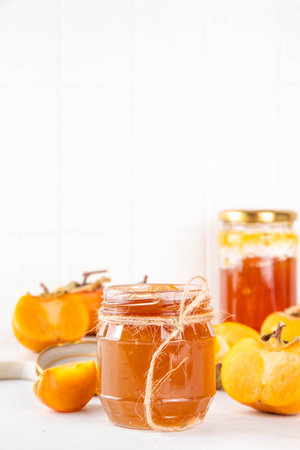Persimmon jam. Sweet autumn homemade jam or marmalade canning preserves in a jar, with whole and cut persimmon c in the backgroundの写真素材