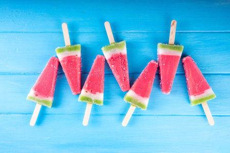Tasty sweet watermelon ice cream lollies on blue wooden table, top view. Summer vacation and holiday background with watermelon fruit popsicles, top view copy spaceの写真素材