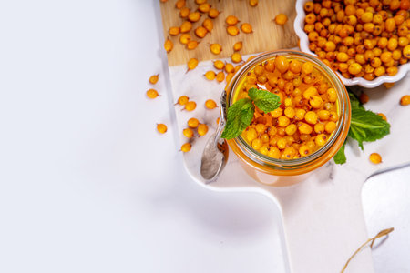 Sea buckthorn jam, homemade jelly preserves in small glass jar with fresh sea buckthorn berries on white marble tableの写真素材