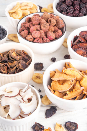 Freeze-Dried Fruits berry, alternative way to store summer harvest. Bowls with dried dehydrated raspberry, blueberry, peach, banana, apricot, plum, blackberry, apple, cherry on white wood backgroundの写真素材