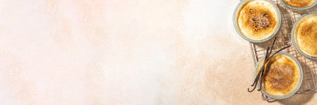 Sweet creme brulee dessert. Portioned glass jars with homemade creme brulee with caramelized sugar crust topping, on beige colored background with sugar in spoon and vanilla copy spaceの写真素材