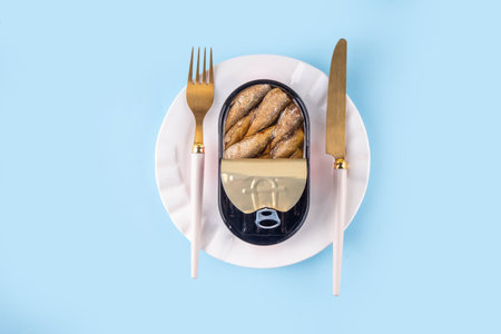 Sardinecore trend concept, canned sardines in metal can on a blue background, on plate with a fork and knifeの写真素材