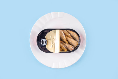 Canned sardines in metal can on a blue background, on plate with a fork and knifeの写真素材