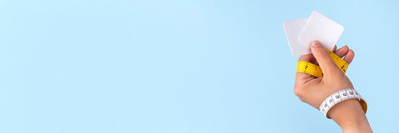 Slim metabolic patches, smart weightloss medical biohacking technology to increase metabolism, energy boost and appetite control. Slim patches with measuring tape and woman hand on blue backgroundの写真素材