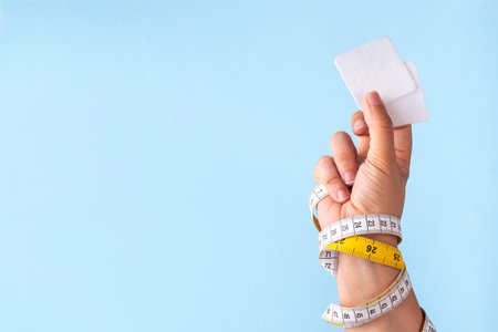 Slim metabolic patches, smart weightloss medical biohacking technology to increase metabolism, energy boost and appetite control. Slim patches with measuring tape and woman hand on blue backgroundの写真素材