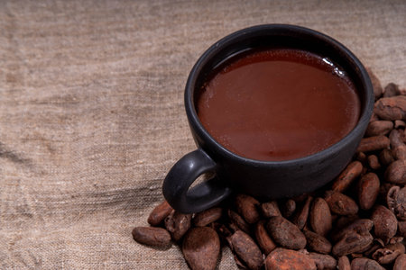 Ceremonial Cacao drink. Hot ceremonial chocolate in black cup with cocoa beans. Woman hands holding...