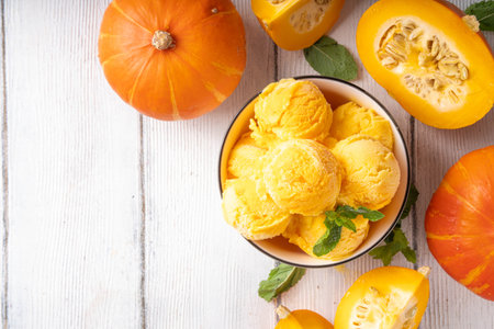 Pumpkin ice cream bowl. Tasty pumpkin squash gelato scoops in portioned bowl, on wooden table with sliced pumpkin squash, copy spaceの写真素材