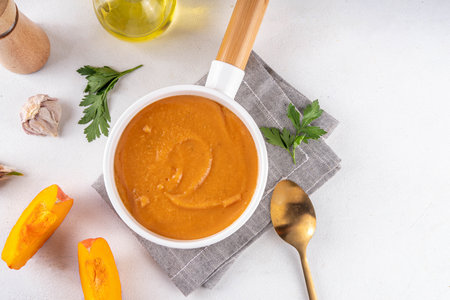Pumpkin cream soup served in white bowl. Traditional fall and winter dishes, hot and spicy pumpkin  soup, creamy and tasty, with pumpkin squash slices and herbs on white tableの写真素材