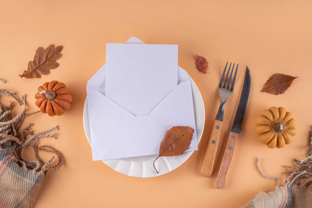 Autumn table setting, party invitation mockup with little pumpkins, fall leaves, plate, cutlery and envelope with an invitation or greeting. Thanksgiving party cozy background copy spaceの写真素材