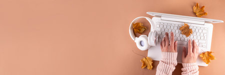 Cozy autumn background with laptop, fall leaves, pumpkins and plaid. Autumn office work, education flat lay top view copy space. Person hands using laptop computer from above on beige backgroundの写真素材