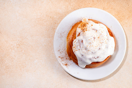Freshly baked homemade cinnamon roll bun with vanilla topping on it, on beige background with spices, copy spacesの写真素材
