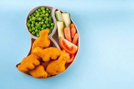 Tasty kids food, dinosaur shaped chicken nuggets. Plate with dino nuggets and sauce and vegetables, healthy and fun air fryied dino nuggetsの写真素材
