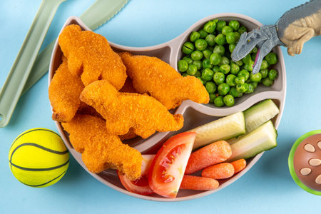 Tasty kids food, dinosaur shaped chicken nuggets. Plate with dino nuggets and sauce and vegetables, healthy and fun air fryied dino nuggetsの写真素材