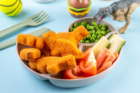 Tasty kids food, dinosaur shaped chicken nuggets. Plate with dino nuggets and sauce and vegetables, healthy and fun air fried dino nuggetsの写真素材