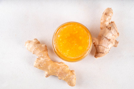 Homemade caramelized ginger jam marmalade preserves in small jar with fresh ginger roots on white table copy spaceの写真素材