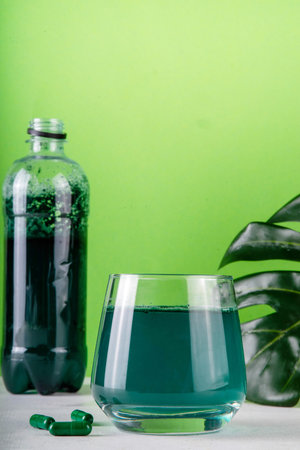 Liquid Chlorophyll Drink. Bottle and Glass with Green Chlorophyll Water, Chlorophyll powder and pills, healthy trendy vitamin beverageの写真素材