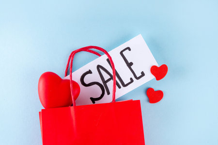 Valentine day sale and shopping background . Red paper shopping bag with text sale, white, red, gold hearts. Simple minimal Valentines greeting card, invitation, marketing promo mockup copy spaceの写真素材