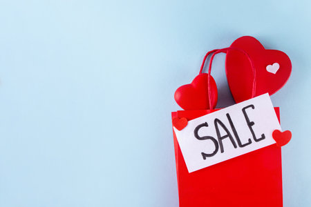 Valentine day sale and shopping background . Red paper shopping bag with text sale, white, red, gold hearts. Simple minimal Valentines greeting card, invitation, marketing promo mockup copy spaceの写真素材