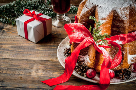 Traditional Italian Christmas fruit cake Panettone Pandoro with festive red ribbon and Christmas decorations, gift box and mulled wine, on wooden home background, copy spaceの写真素材