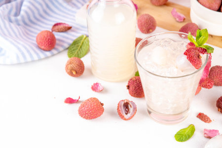 Lychee fruit tasty margarita or lemonade cocktail. Tasty alcohol drink with fresh lychees, mint leaves, liqueur and sweet sour juice, on white pink table background with ripe raw lychee fruits, copy spaceの写真素材
