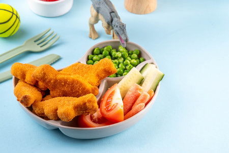 Tasty kids food, dinosaur shaped chicken nuggets. Plate with dino nuggets and sauce and vegetables, healthy and fun air fryied dino nuggetsの写真素材