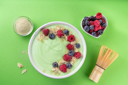 Green matcha yogurt bowl with fresh berries, nuts and granola. Tasty healthy smoothie bowl for...