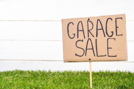 Spring garage sale background. Decluttering, selling unnecessary things backyard market - wooden box  with old clothes, toys, dishes, stuff and sign Garage Sale on sunny grass wooden background