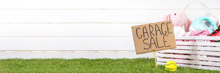 Spring garage sale background. Decluttering, selling unnecessary things backyard market - wooden box  with old clothes, toys, dishes, stuff and sign Garage Sale on sunny grass wooden background