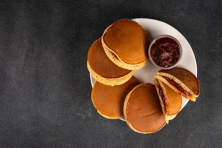 Dorayaki, classic Japanese pastry, golden honey pancake sandwich filled with sweet red bean paste or sweet berry jam. Sponge cake dessert cooked in frying panの写真素材