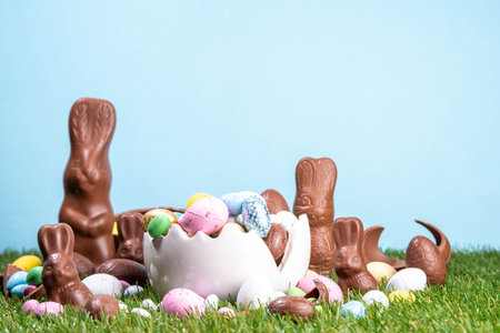 Easter egg hunting background with chocolate eggs. Various candy and chocolate Easter eggs, bunny and rabbits with basket for eggs on green grass park or garden backgroundの写真素材