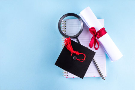 Happy graduation day background. Graduation themed accessories - rolled diploma with red ribbon, graduation cap, books and notebook for preparing for exams, keyboard, eyeglasses and pen