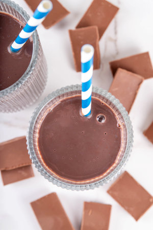 Chocolate milk or chocolate milkshake drink. Two tall glasses with cocoa beverage, yogurt, milk or milkshake with slices of chocolate and striped drinking straws, copy space