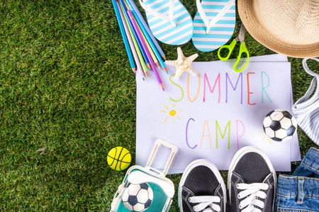 Kids summer camp invitation background. Bright yellow backdrop with Summer Camp ad text banner, pencils, summer shoes, flip-flops, ball, sneakers, sand toys, summer hat, suitcase, on grass background
