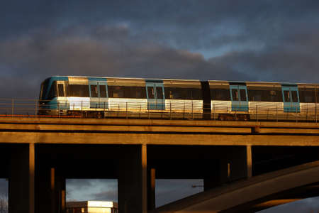 A subway train on a bridge with good sunshine and dark cloudy background