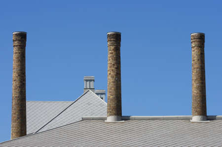 three chimneys on a rooftop with a blue skyの写真素材