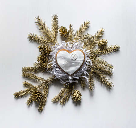 Christmas gingerbread cookies in the form of hearts with white icing lies in the center on the golden fir branches and conesの写真素材