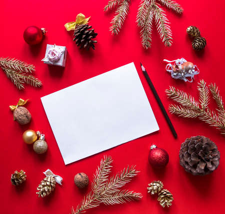 on a red raspberry background, New Year and Christmas decorations and spruce gold branches are arranged in a circle, and in the center lies a white sheet and a pencilの写真素材