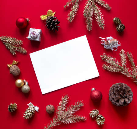 on a red raspberry background, New Year and Christmas decorations and spruce gold branches are arranged in a circle, and in the center lies a white sheet and a pencilの写真素材